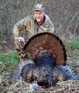 Fred Clark dressed in camouflage, standing behind a turkey.